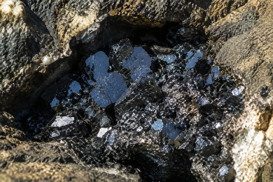 Black zinc ore crystals sparkling in a rocky crevice with natural sunlight.