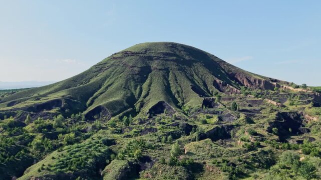 Aerial counterclockwise orbit around a rugged volcanic cinder cone with deep eroded gullies under clear daylight.