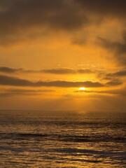 Fototapeta premium Vertical photography of intense golden orange sunset sun rays breaking through sky clouds over ocean in La Jolla, CA.