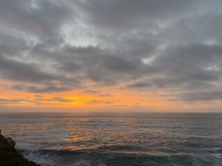 Fototapeta premium Wide vista of brilliant orange afterglow along the ocean horizon under dark overcast evening clouds in La Jolla, CA.