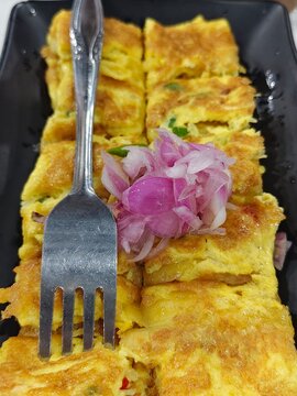 golden-brown egg omelet or egg roll (telur dadar) served on a black rectangular plate.