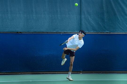 Young Asian Male Tennis Player Hitting a Powerful Serve on Outdoor Court