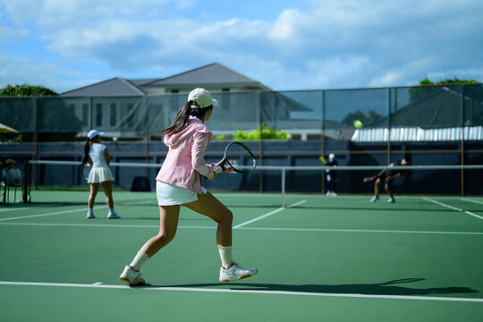 Young Asian Woman Playing Tennis on Outdoor Green Court During Sunny Day Doubles Match