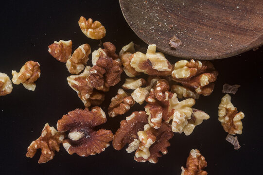 Macro of walnut kernels spread on a black background beside a wooden spoon