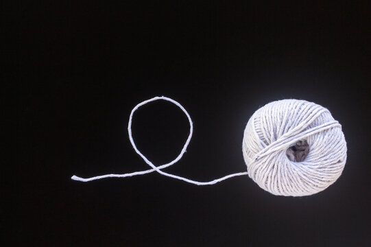 White yarn ball with a looped thread on a black background
