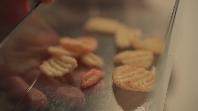 Close up of hands reaching into transparent container to pick up small ridged. Scene focuses on texture and color variations. Reflections from glass surfaces add depth