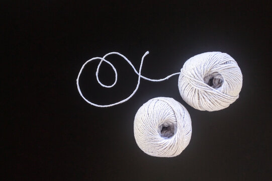 Two balls of white yarn with curled thread on a black background
