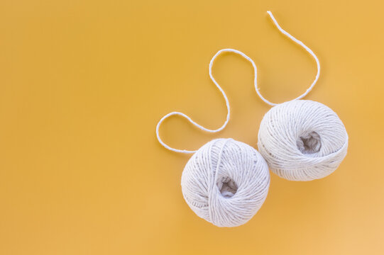 Two balls of white yarn with curved thread on a yellow background