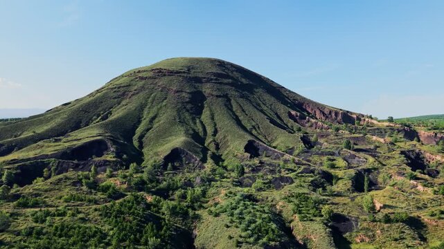 Epic aerial tracking shot of a majestic volcano cinder cone with deep gullies and dramatic shadows. Mysterious and rugged geological formations under a clear blue sky.