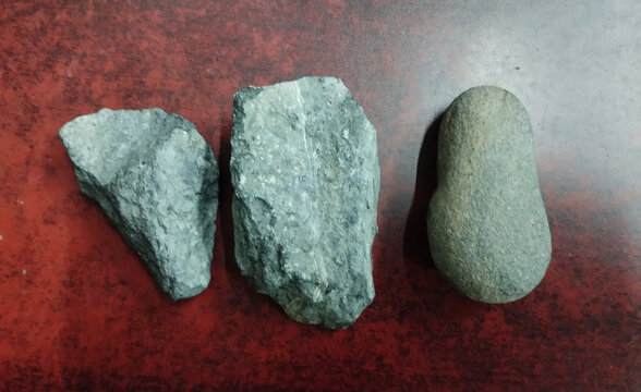 Three natural stones with rough textures and earthy greenish-gray hues on dark surface.