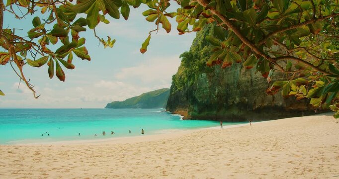 People swim in turquoise water at Kelingking Beach under green cliffs in Nusa Penida Bali