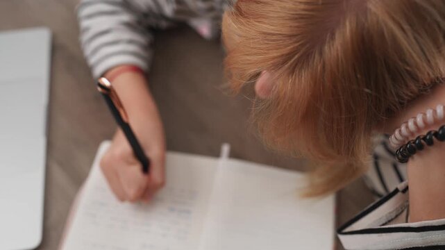 Student writing in notebook. Woman taking notes in diary with pen. Girl studying and handwriting a letter or an essay. Education, learning and journaling concept from top view