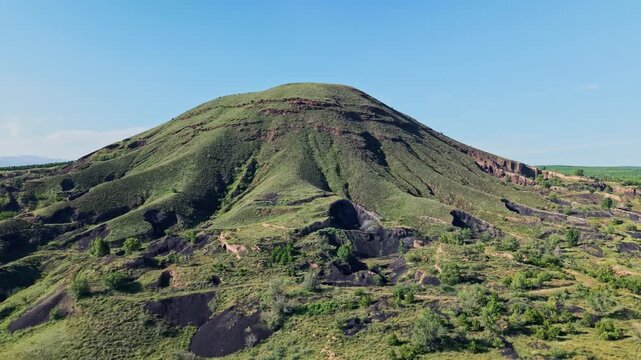 Aerial counterclockwise orbit of a rugged volcano cinder cone with deep dramatic shadows defining eroded gullies under bright sunlight.
