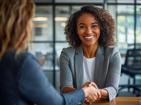 Two professionals shaking hands across a wooden table in a modern glass-front office conveying confidence and a friendly agreement