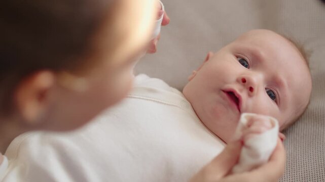 Mom playing and kissing with a newborn baby. Cute baby is trying to pronounce sounds while looking at his mom. Face of an active Caucasian baby looking at a parent.  Mom is  kissing her baby.