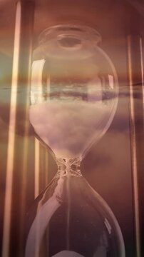 Close up of sand falling through a glass hourglass, double-exposed with a sunset sky. Depicts passing time, investment duration, deadlines, and urgency.
