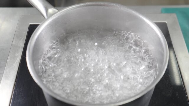Hot boiling water in large stainless steel pot on stove. Dense rising steam, strong bubbles, professional kitchen cooking process for meal preparation Slow motion 4k video