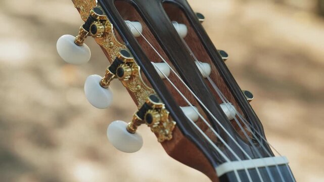 Close-up of the guitar head of a classical guitar with gold pegs. Part of a classical guitar on a blurry background in the park. Head of guitar with nylon strings. Slow motion 4k footage.