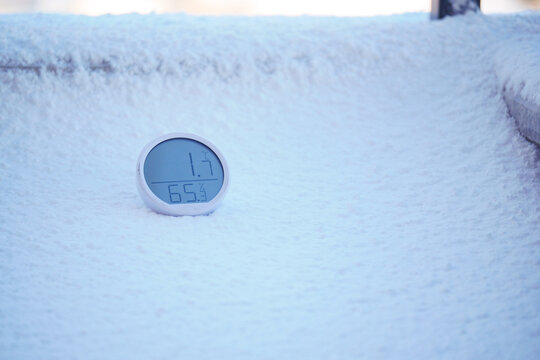 round white digital thermometer and hygrometer sitting on a snowy surface