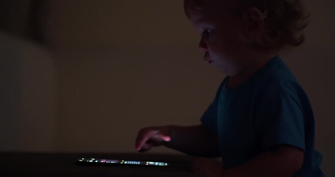 Baby pressing and  tapping with finger on phone touch screen.  Child is scrolling on mobile phone. Little child learns to use new  technologies. Baby plays with cellphone at home in the evening
