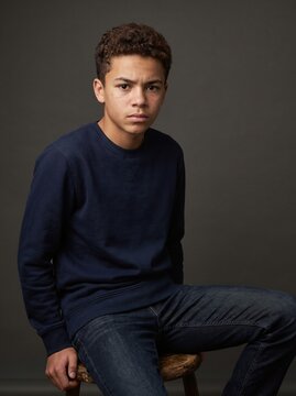 Young man sitting on a rustic wooden stool in a professional studio portrait