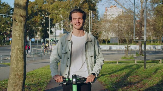 Young smiling man rides an electric scooter in the city on a sunny day. Happy student riding on a rented green electric scooter through the streets of the city. Ecological transport. Slow motion
