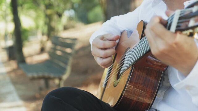 Professional guitarist plays guitar outdoors. Musician plays a classical guitar in the park. A man in a white shirt plays a musical instrument outside the house. The guitarist plays the guitar.