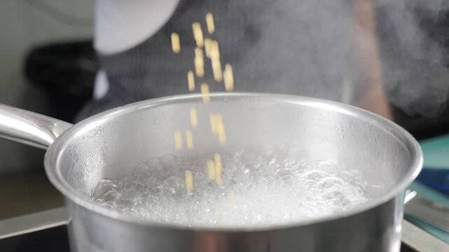 Chef hand dropping ptitim pearls into pot of boiling water. Steam rising, professional restaurant kitchen cooking process, preparing traditional Israeli couscous dish Slow motion 4k video