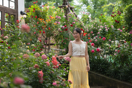 Asian woman turning around smiling in blooming rose garden cafe.