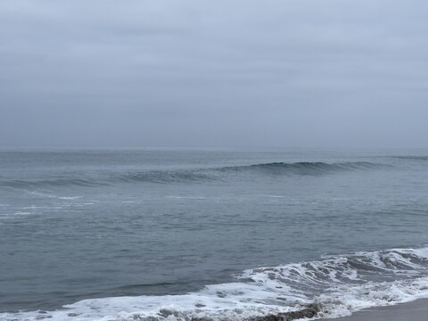 Calm ocean swells rolling over gray waters toward Carlsbad beach under overcast morning skies in California.