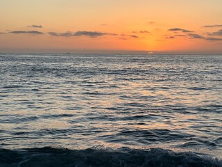 Obraz premium Vibrant orange sunset over calm ocean waters in Carlsbad, California with distant boat outline on horizon.