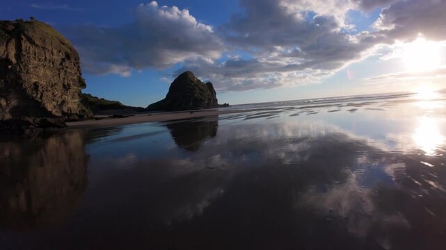 Sunset reflections on wet sand at Piha Beach, New Zealand