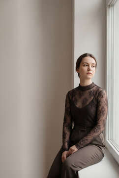 Young woman in lace top sitting by window in contemplation