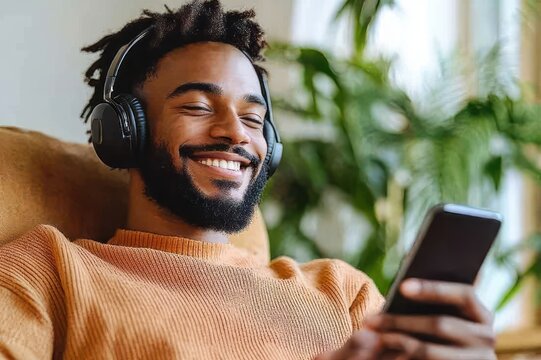 relaxed person reclining on a sofa wearing headphones and an orange sweater, content while using a smartphone with indoor plants in the background