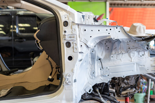 Disassembled white car body undergoing structural repair an automotive workshop exposed frame engine bay interior during professional restoration service