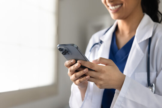 Cropped closeup view of South Asian female doctor texting on smartphone in clinic. Digital communication in healthcare, telemedicine application use, remote medical consultations of patient concept