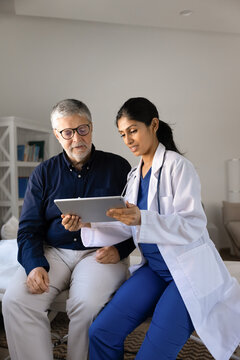 Female doctor reviewing digital test results on tablet with male patient, explaining health information, sharing treatment plan at hospital. Professional healthcare consultation, telemedicine app use