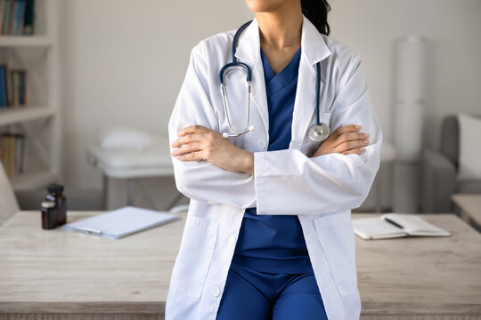 Closeup cropped view unknown female physician in coat and stethoscope poses with arms crossed in clinic office examination room. Professional medical services, healthcare, wellness industry concept