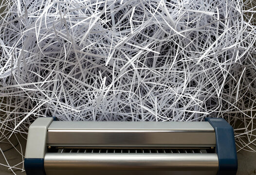 Data security and privacy protection, paper shredder with shredded documents for corporate compliance and information destruction in a business office