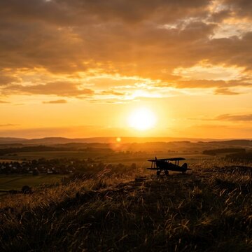 Vintage Biplane Silhouetted Against a Dramatic Sunset Over Rolling Hills.