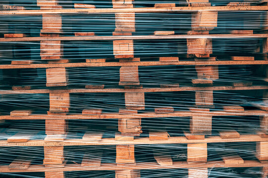 Stacked weathered EUR pallets secured with transparent plastic wrapping in front of a warehouse building. Shipping, inventory management and commercial distribution theme.