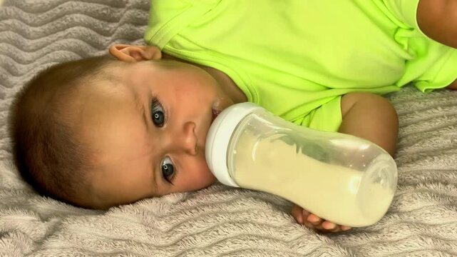 Infant drinks formula from a bottle while lying on a bed at home, baby nutrition, early development and peaceful feeding routine.