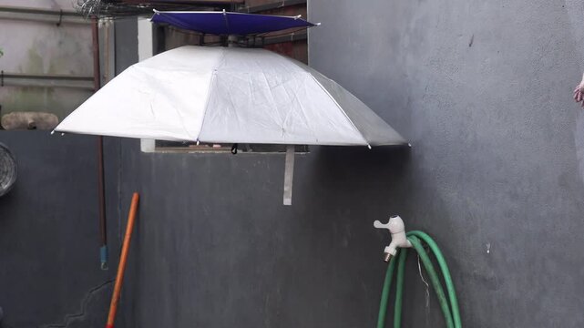 Medium shot of a silver fishing umbrella hanging outdoors on a concrete wall.