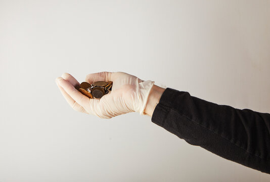 A man's hand in a white medical glove holds money in the form of small coins. Protection against viruses and bacteria. Concept. Covid-19 or Coronavirus.