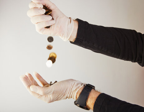 Hands of a man in white medical gloves pour money in the form of small coins from one hand to another. Protection against viruses and bacteria. Concept. Covid-19 or Coronavirus. Selective focus.