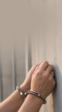 Hands in steel handcuffs leaning against a concrete wall