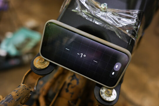Mobile application for measuring planes displays negative angle on smartphone mounted to mechanical equipment, with industrial wear and blurred workshop background
