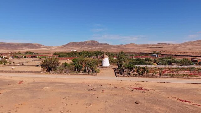 Aerial view of surroundings from El Cotillo, a coastal town located on the island of Fuerteventura, Canary Islands, Spain. Drone POV of windmill and car passing on the dirt road,