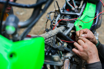 Fototapeta premium Motorcycle repair, mechanic hands, electrical wiring, green body panel, and exposed engine components during detailed vehicle maintenance work in outdoor workshop setting