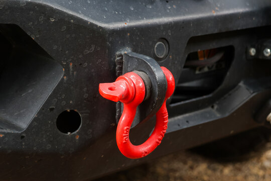 Red towing shackle attached to rugged black vehicle bumper for off road recovery, showing durable metal hardware, mechanical detail, and outdoor adventure equipment
